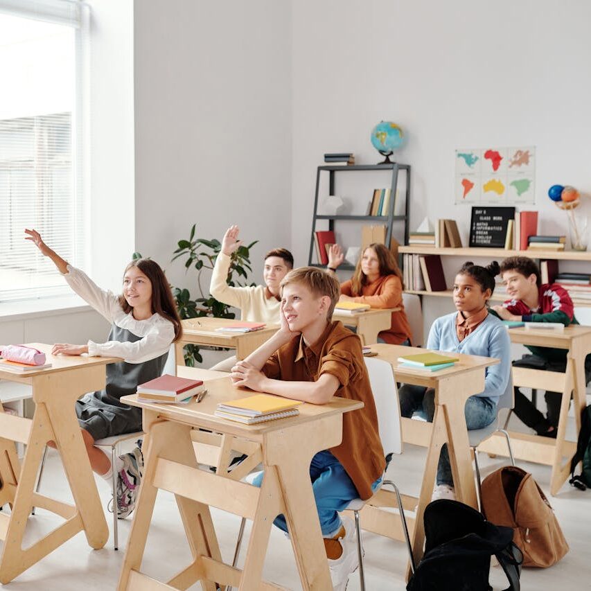un profesor dando clase a unos niños. Algunos de esos niños tienen la mano levantada